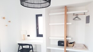 A modern, minimalistic room with a white desk, a black chair, a wooden shelf unit, and a hanging light fixture. - Luxury hospitality, outstanding view (Thira - Santorini)