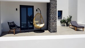 A modern outdoor seating area with a hanging chair, a lounge chair, and a potted plant. - Luxury hospitality, outstanding view (Thira - Santorini)