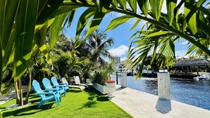 A waterfront patio with green artificial grass, lounge chairs, and a concrete pathway leading to a water body. - Waterfront Home Steps to Beach (Fort Lauderdale)