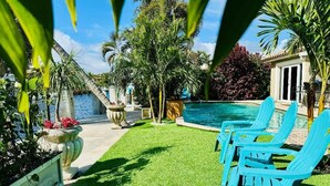 A backyard with a swimming pool, green artificial grass, and blue lounge chairs. - Waterfront Home Steps to Beach (Fort Lauderdale)