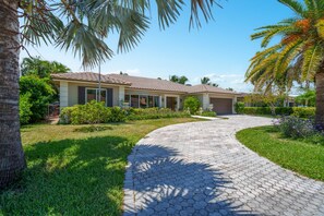 A residential property with a paved driveway, surrounded by lush greenery and palm trees.