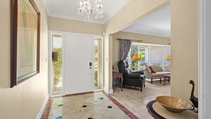 A spacious hallway with a tiled floor, a chandelier, a dining area with a sofa and table, and a decorative bird sculpture. - Waterfront Home Steps to Beach (Fort Lauderdale)