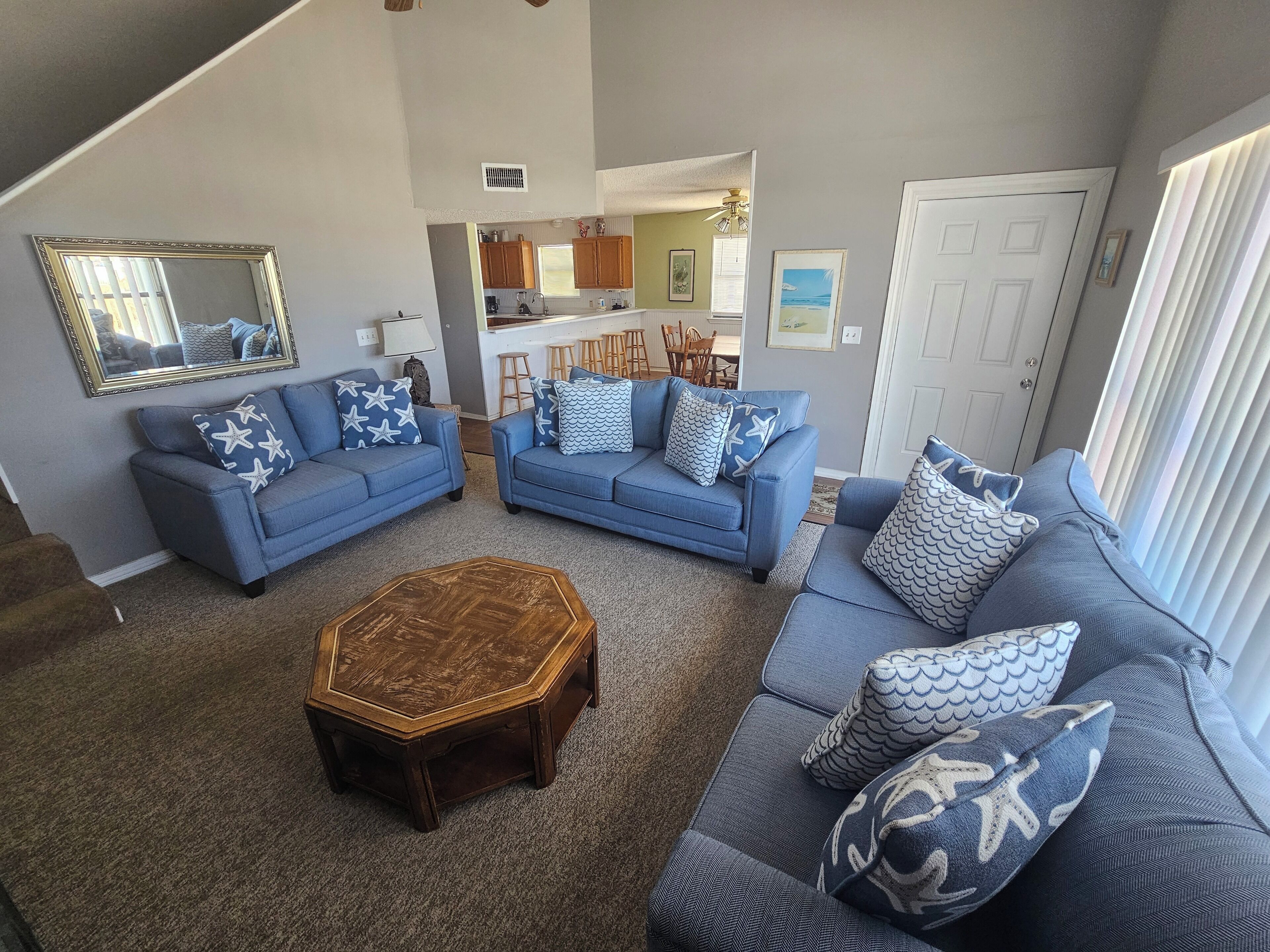 A living room with two blue sofas, a wooden coffee table, and a staircase leading to a kitchen.