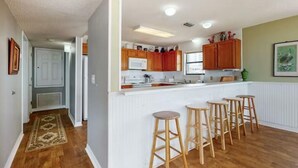 A kitchen with wooden cabinets, a white countertop, and bar stools. - Beachfront - Great Location! (Gulf Shores)