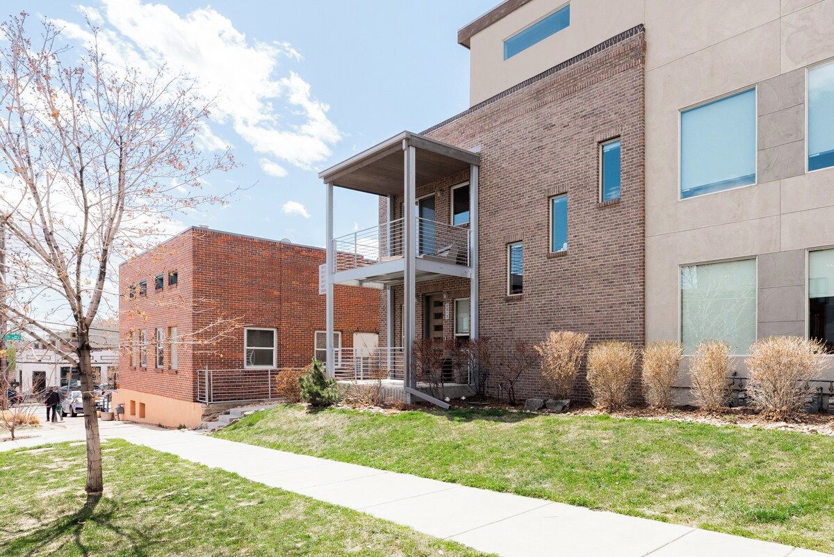 Un bâtiment moderne avec une façade en briques, un espace extérieur couvert et une cour verdoyante.