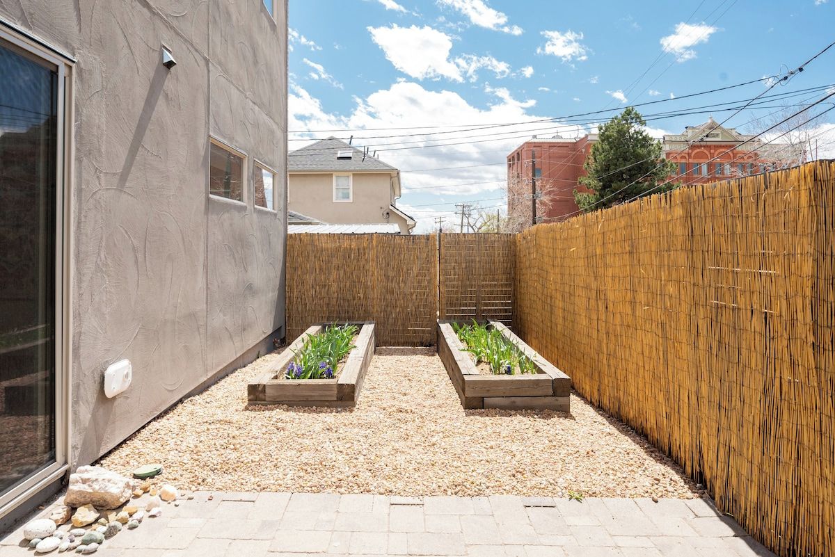 Un petit espace jardin aménagé avec des plates-bandes surélevées, une clôture en bois et un chemin pavé.