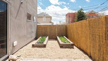 A small garden area with raised beds, a wooden fence, and a paved walkway.
