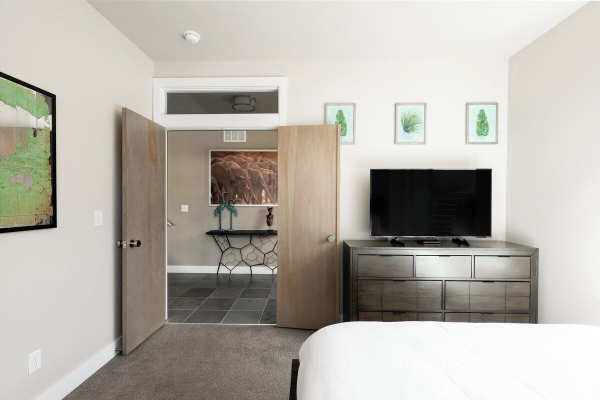 Una habitación de hotel con cama, televisión, cómoda y puerta que da a un baño.