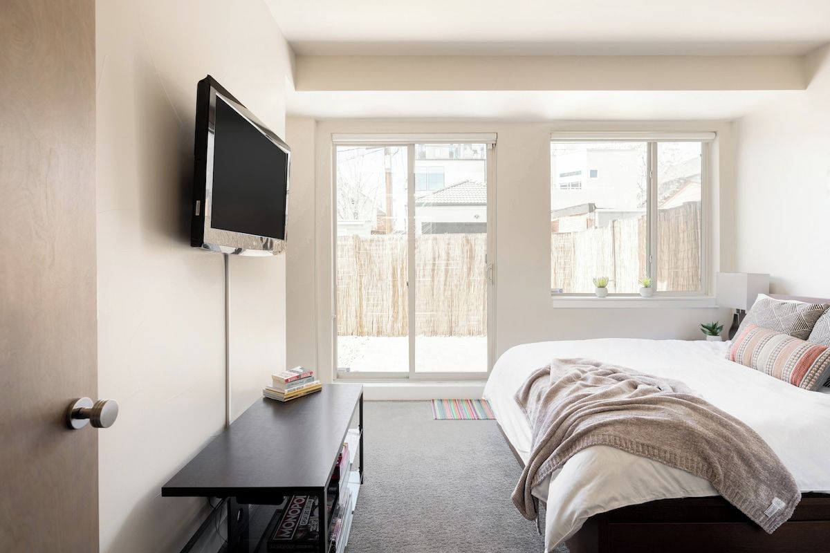 Une chambre à coucher avec un lit, un téléviseur fixé au mur, un bureau et une fenêtre donnant sur l’extérieur.