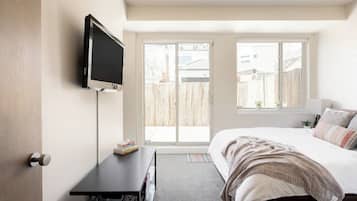 Une chambre à coucher avec un lit, un téléviseur fixé au mur, un bureau et une fenêtre donnant sur l’extérieur.