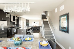 A modern kitchen with a dining area, a staircase, and a large mirror on the wall.