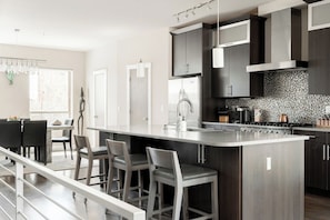 Een moderne keuken met donkere kastjes, een groot eiland met barstoelen en uitzicht op de eetruimte.