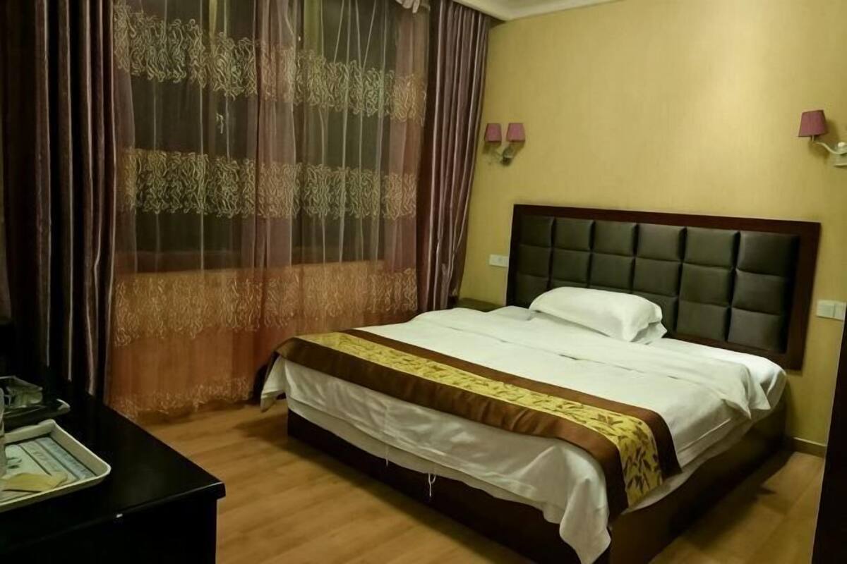 A hotel room with a bed, curtains, a bedside table, and a lamp.