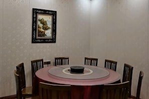 A round dining table with six chairs, a framed artwork on the wall, and a patterned wallpaper.