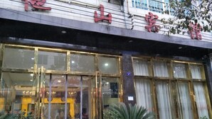 Entrada de hotel con amplias puertas y ventanas de vidrio, plantas en macetas al frente y un letrero con caracteres chinos.