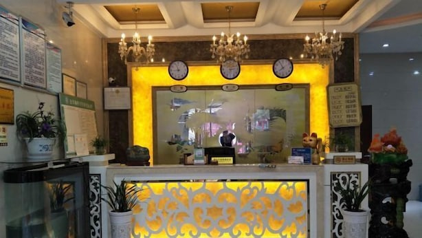 Zona de recepción de un hotel con mostrador, candelabros, relojes y plantas decorativas.