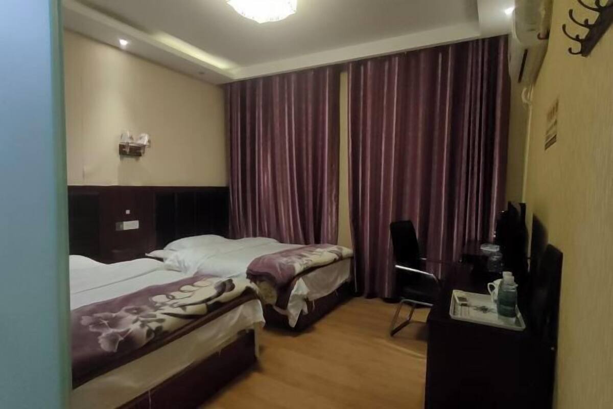 A hotel room with two beds, a desk, a chair, and a TV.