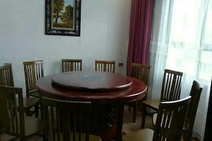 A dining area with a round table surrounded by wooden chairs, a framed picture on the wall, and a window with curtains.