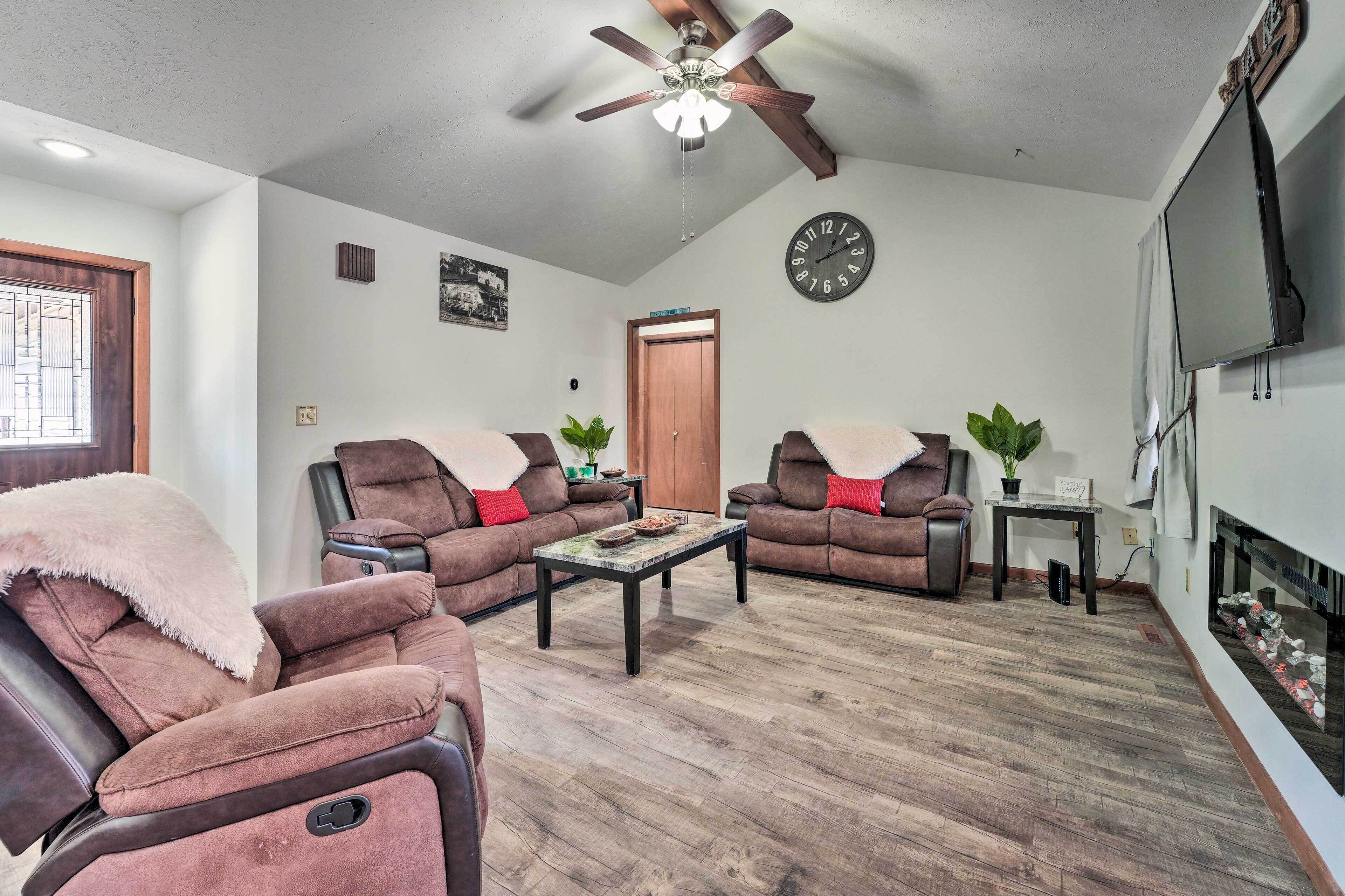 A living room with two brown sofas, a coffee table, a ceiling fan, a clock, and a fireplace.