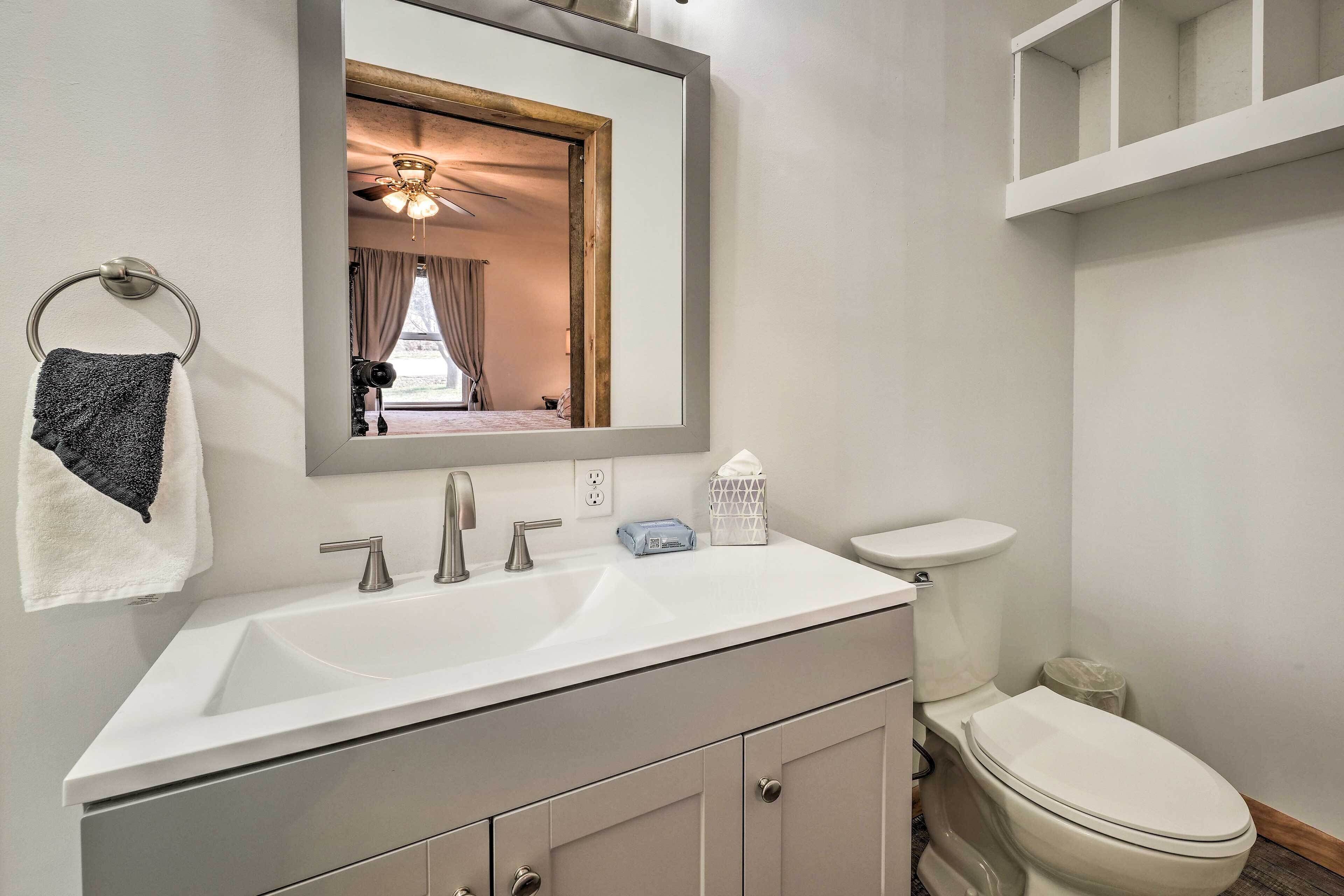 Une salle de bain avec un lavabo blanc, un miroir, un porte-serviettes, des toilettes et un ventilateur de plafond.