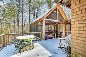 A wooden deck with a table and chairs, surrounded by snow-covered ground and trees.