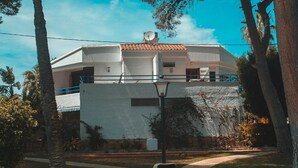 Un edificio blanco con techo de tejas, rodeado de árboles y un sendero de piedra.