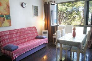 Une pièce chaleureuse avec un canapé rouge à motifs, une table à manger avec des chaises, une horloge et une fenêtre avec des rideaux.