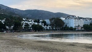 Una playa con orilla arenosa y mar tranquilo. Al fondo, se observan edificios blancos de varios pisos y balcones.