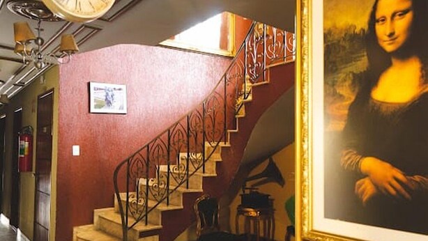 Una escala amb barana de metall decorada, un quadre emmarcat de la Mona Lisa i un rellotge a la paret.