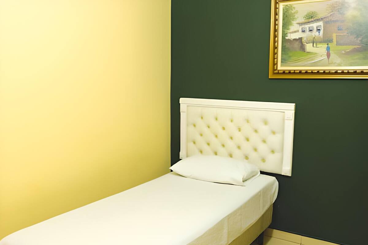 A single bed with a tufted headboard in a room with green walls and a yellow accent wall.