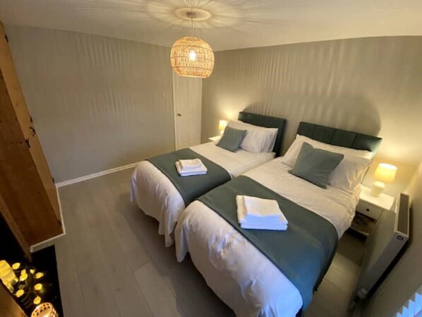 A hotel room with two beds, a chandelier, and a nightstand with a lamp.