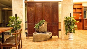 A lobby with a marble floor, wooden furniture, and potted plants.