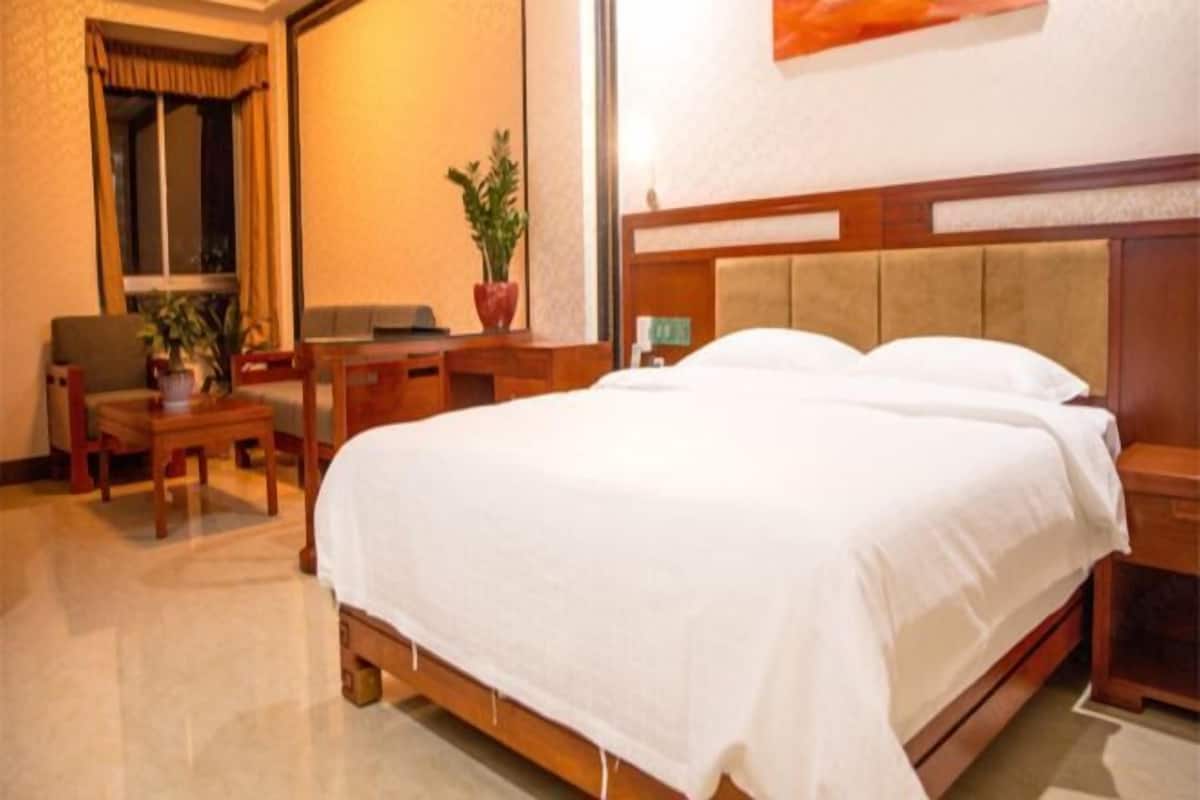 Ein Hotelzimmer mit einem Bett, einem Schreibtisch, einem Stuhl, einer Zimmerpflanze und einem Vorhangfenster.