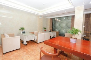 Un área de comedor de hotel con mesa de madera, asientos acolchados y plantas en macetas.