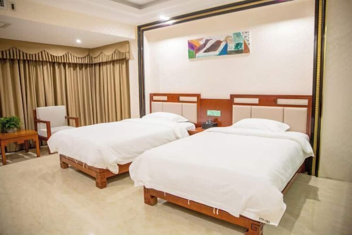 Ein Hotelzimmer mit zwei hölzernen Betten, einem Sessel, einem kleinen Tisch und einem Bild an der Wand.