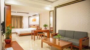 A hotel room with a bed, a sofa, a coffee table, a desk, and a TV.
