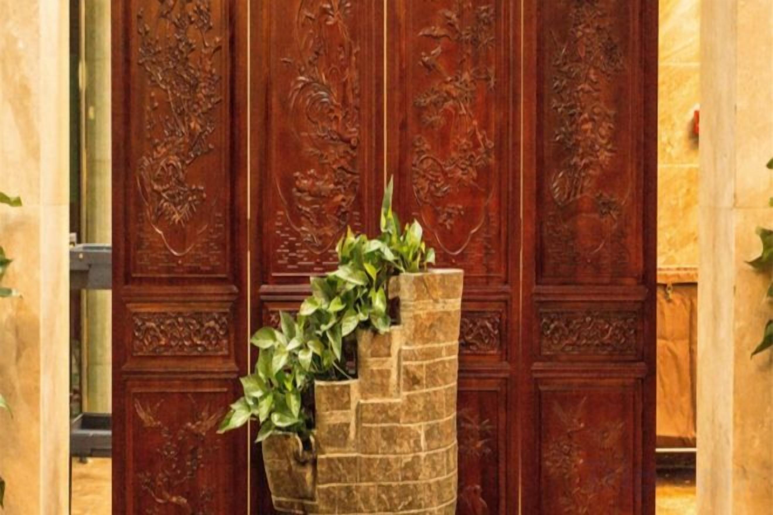 Una puerta de madera con elaborados grabados y una jardinera de piedra con follaje verde.