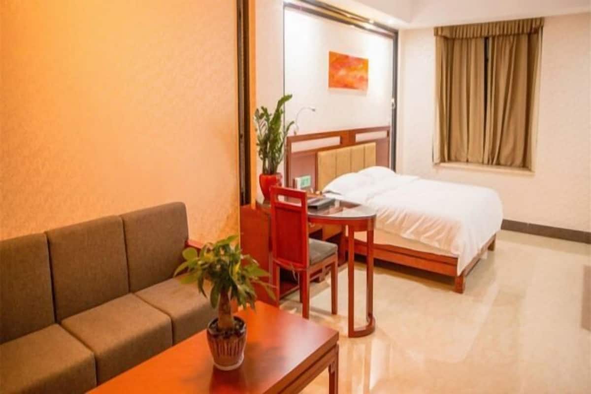 Ein Hotelzimmer mit einem Bett, einem Holztisch, einem roten Sessel, einer Couch und einem Blumentopf.