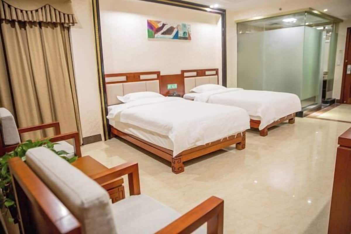 Ein Hotelzimmer mit zwei Betten, einem Holzkopfende, einem kleinen Tisch und einem Stuhl.