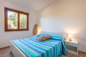 A bedroom with a bed, a nightstand, a lamp, a window, and a wall-mounted light fixture.