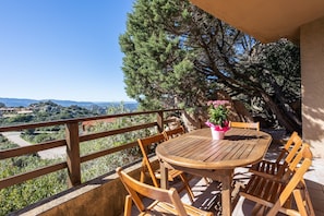 A wooden table and chairs on a balcony with a view of the landscape.