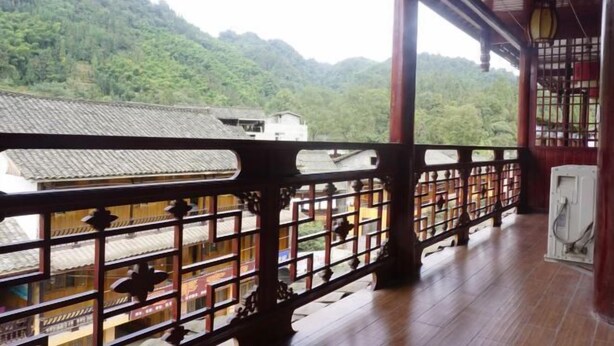 A traditional wooden balcony with a view of a village and forested hills. - Haiyue Hotel (Ya'an)