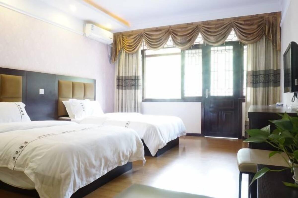 A hotel room with two beds, a desk, a television, and a window with curtains.