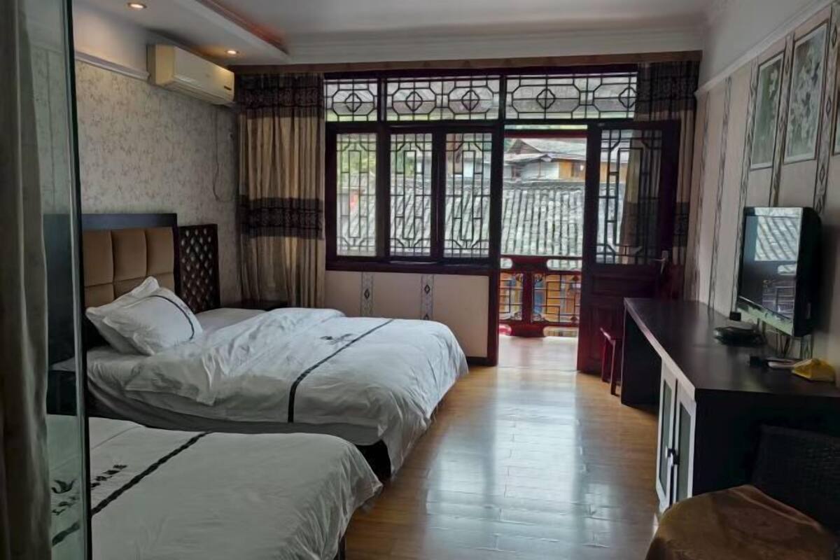 A hotel room with two beds, a TV, a desk, and a view of the outside.
