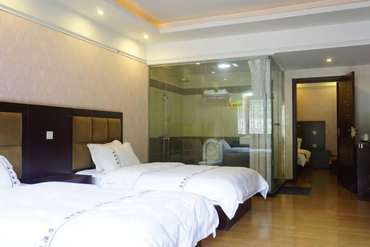 A hotel room with two beds, a glass shower enclosure, and a visible bathroom.