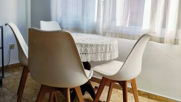 Un coin repas avec une table et des chaises, une fenêtre ornée de rideaux légers et un sol carrelé.
