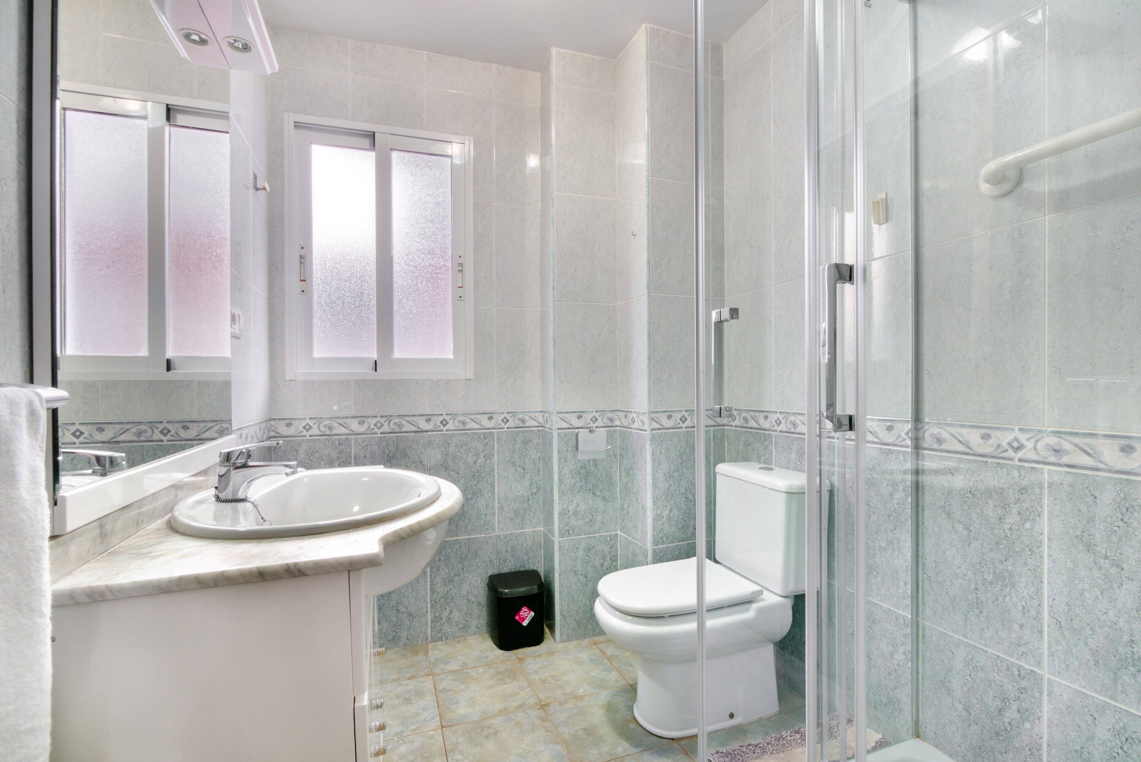 Un baño con ducha envuelta en vidrio, un lavamanos y un inodoro.