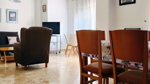 Een woonkamer met een bank, stoelen, een televisie en een eettafel.