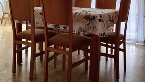 Een eethoek met een tafel voor zes personen, omringd door houten stoelen, een hanglamp en een raam met dunne gordijnen.
