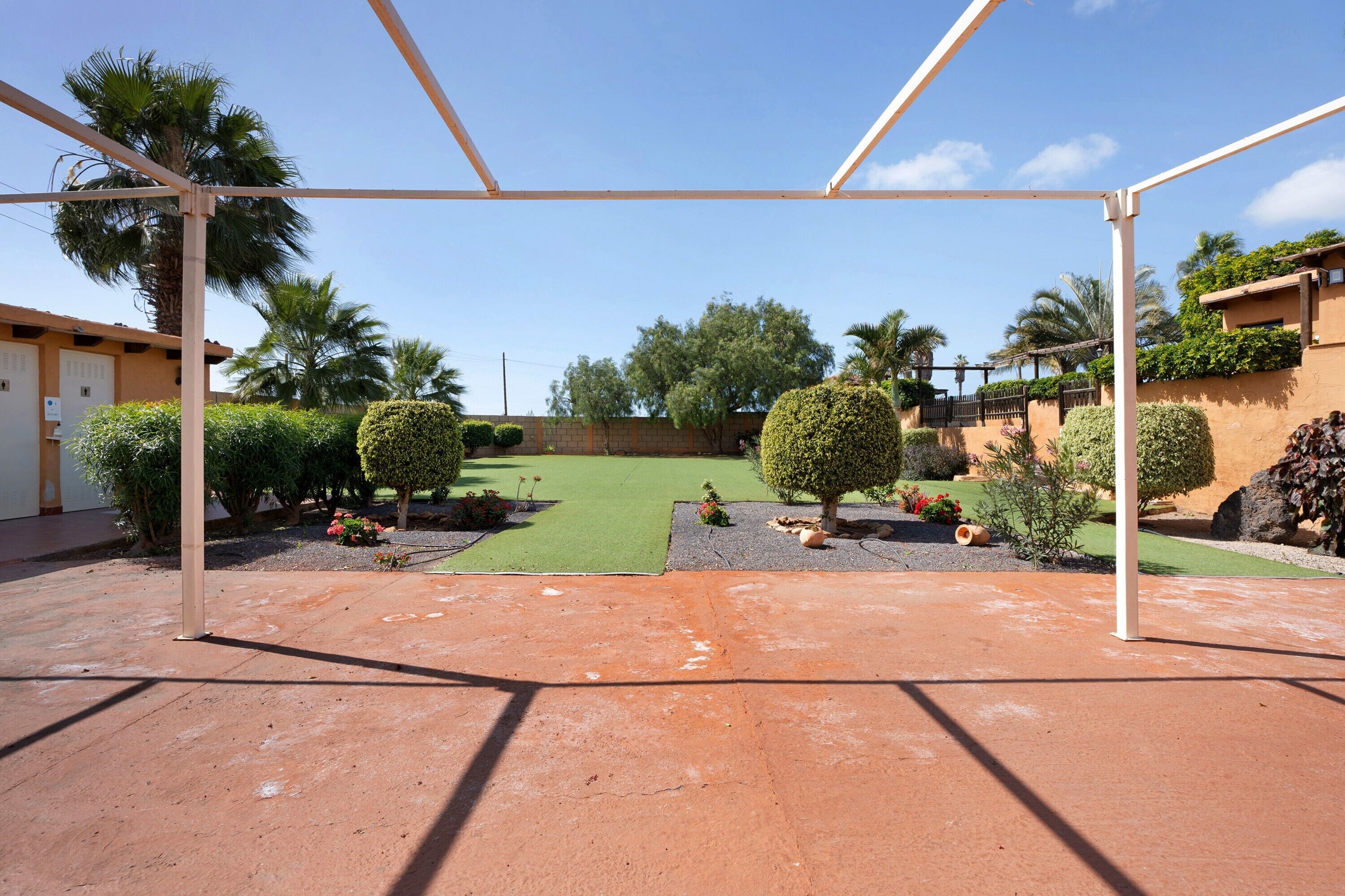 A covered patio area with a green lawn, palm trees, and a clear sky.